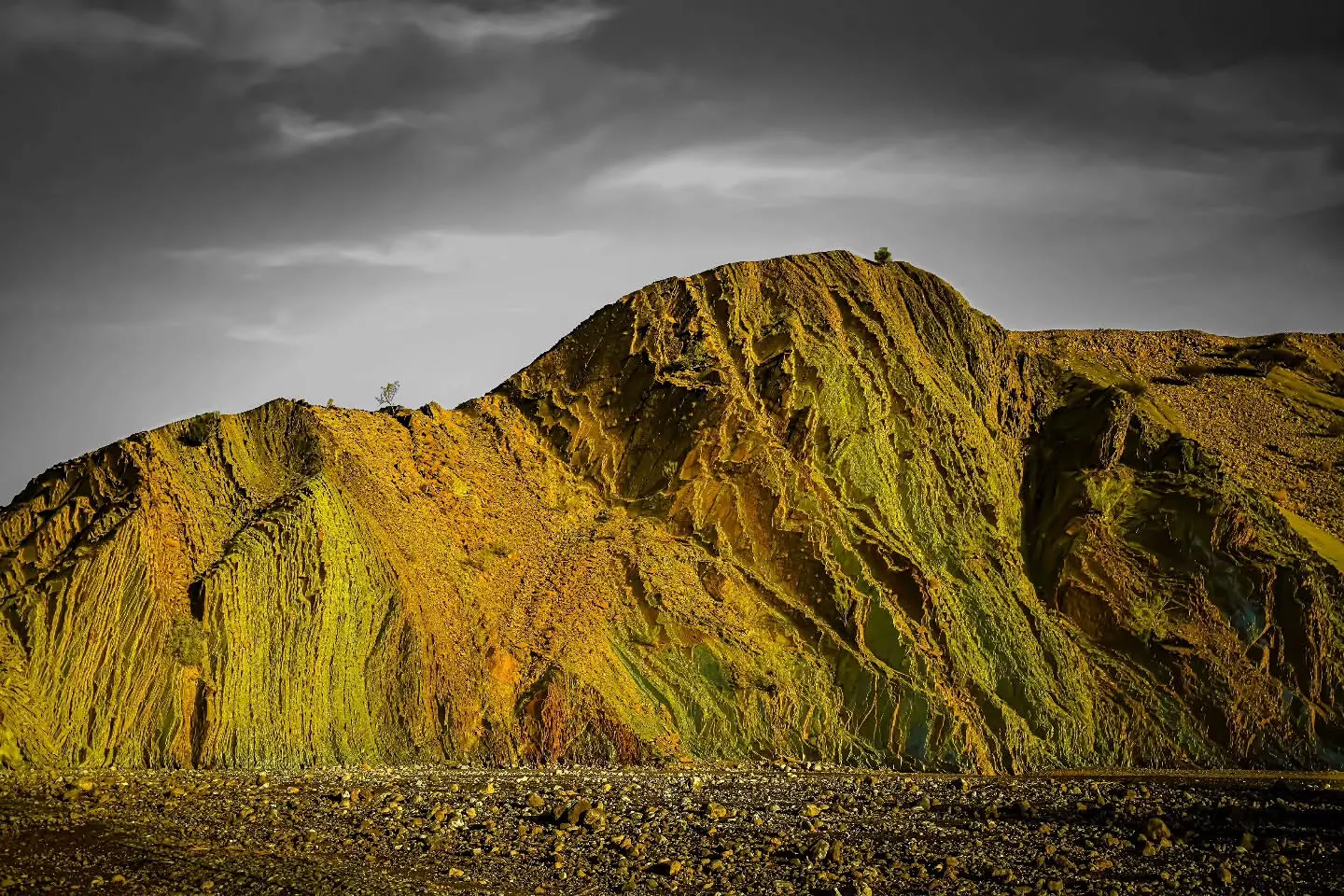 Selective yellow colour brings out the sharp folds of a mountain beneath a grey sky.