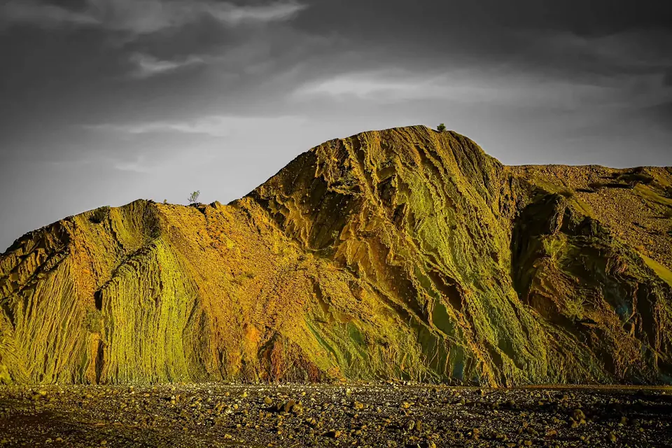 Selective yellow colour brings out the sharp folds of a mountain beneath a grey sky.