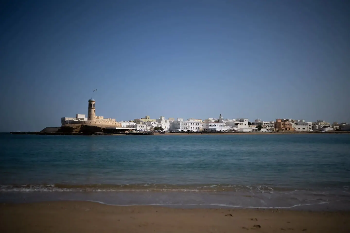 A white waterfront settlement stretches along a blue bay beneath a clear sky.