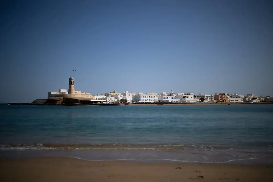 A white waterfront settlement stretches along a blue bay beneath a clear sky.