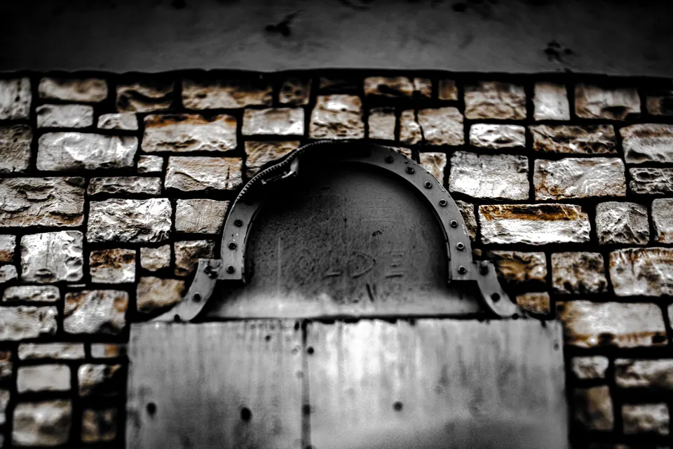 A stone arch frames a boarded opening in a rough masonry wall.