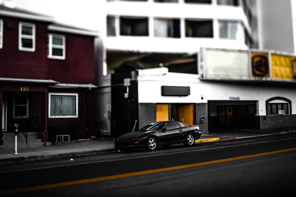 Old storefronts and a parked dark car line a quiet city street.