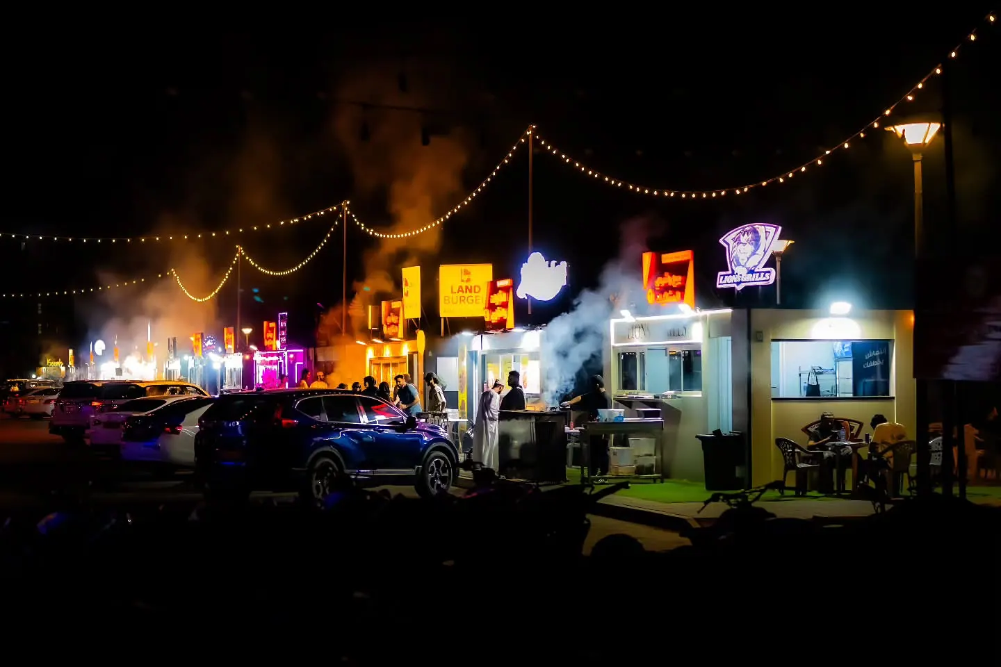 Strings of lights and glowing shop signs brighten a busy street at night.