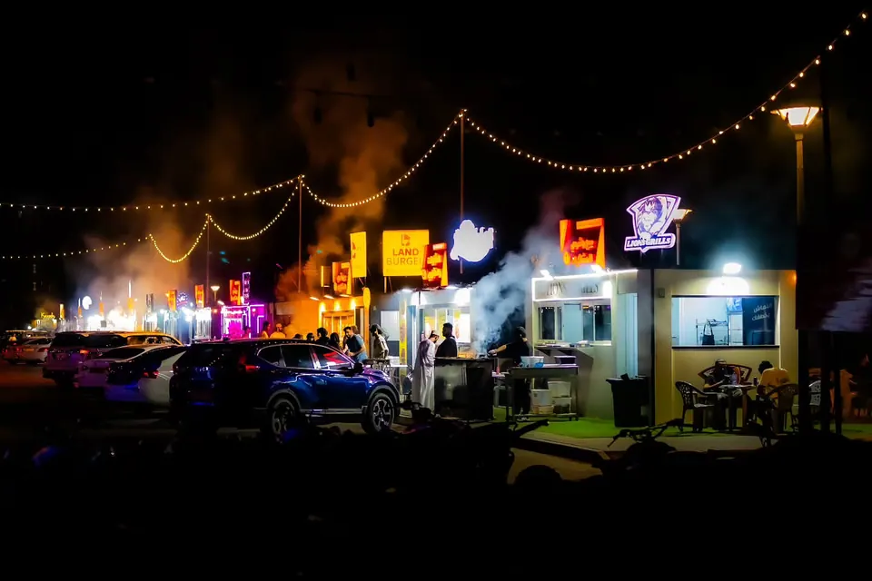 Strings of lights and glowing shop signs brighten a busy street at night.