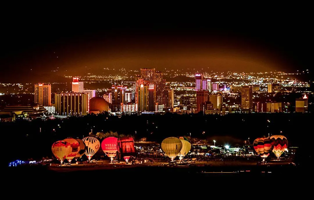 Illuminated balloons line up below a brightly lit city skyline at night.