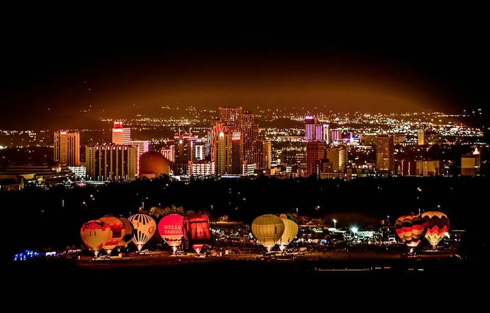 Illuminated balloons line up below a brightly lit city skyline at night.