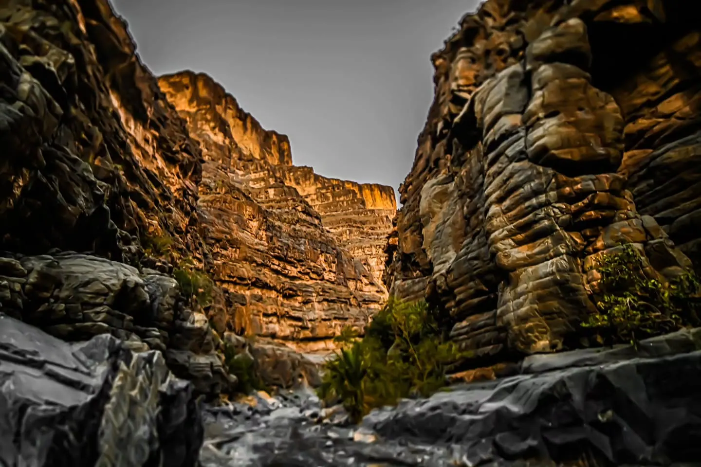 Steep, layered rock walls enclose a narrow gorge scattered with boulders.