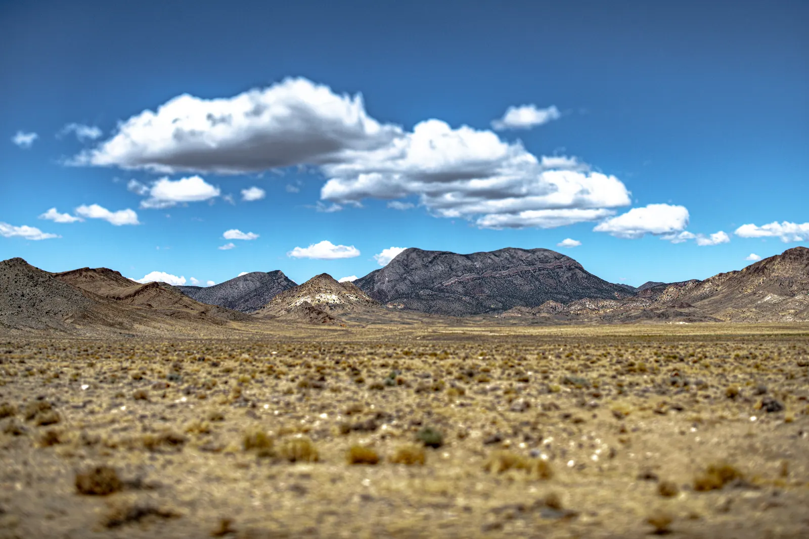 Dry grass stretches toward layered mountains beneath scattered white clouds.