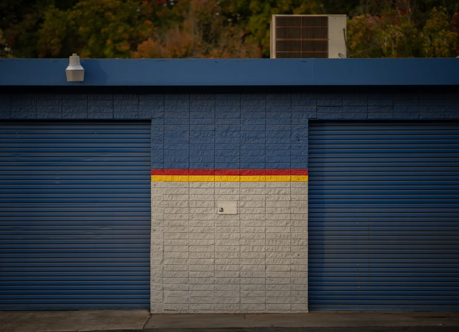 Closed blue shutters and a narrow coloured stripe form a quiet geometric facade.