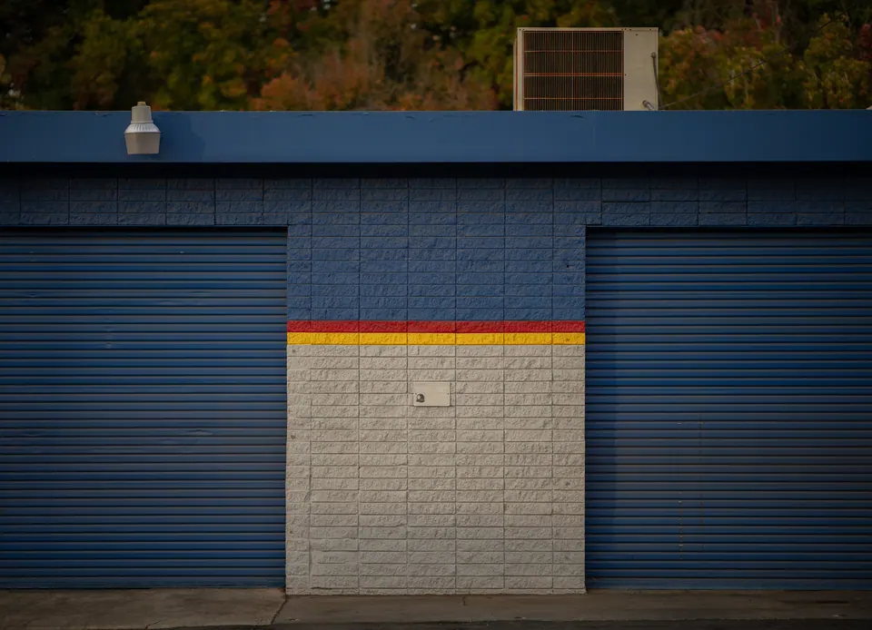 Closed blue shutters and a narrow coloured stripe form a quiet geometric facade.