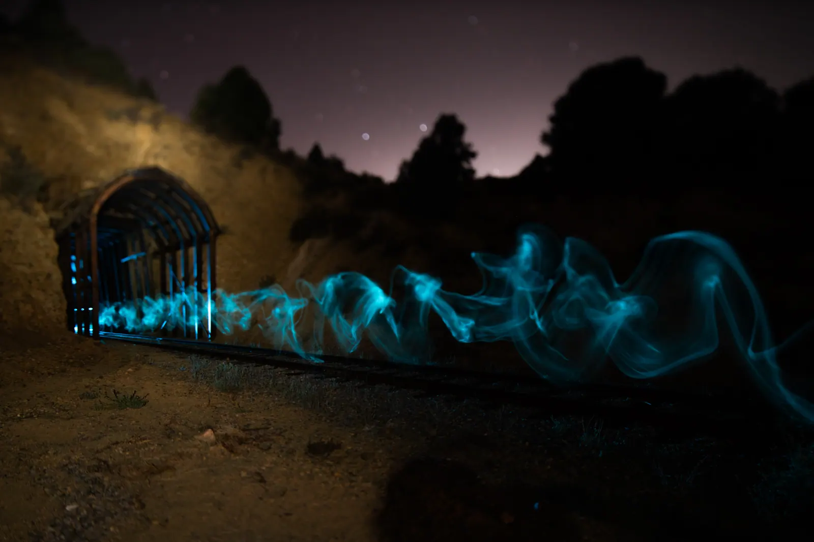 A ribbon of blue light crosses the foreground of a small structure under the stars.