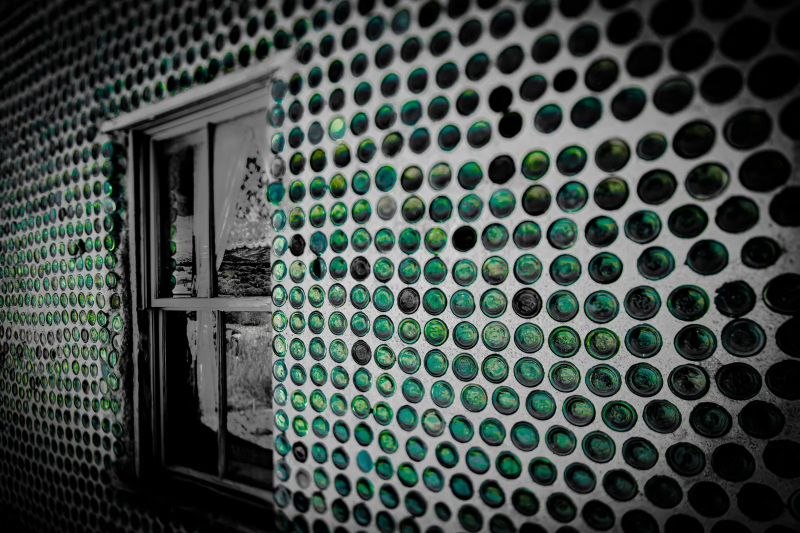 Rows of green glass bottles embedded in a wall surround a dark doorway.
