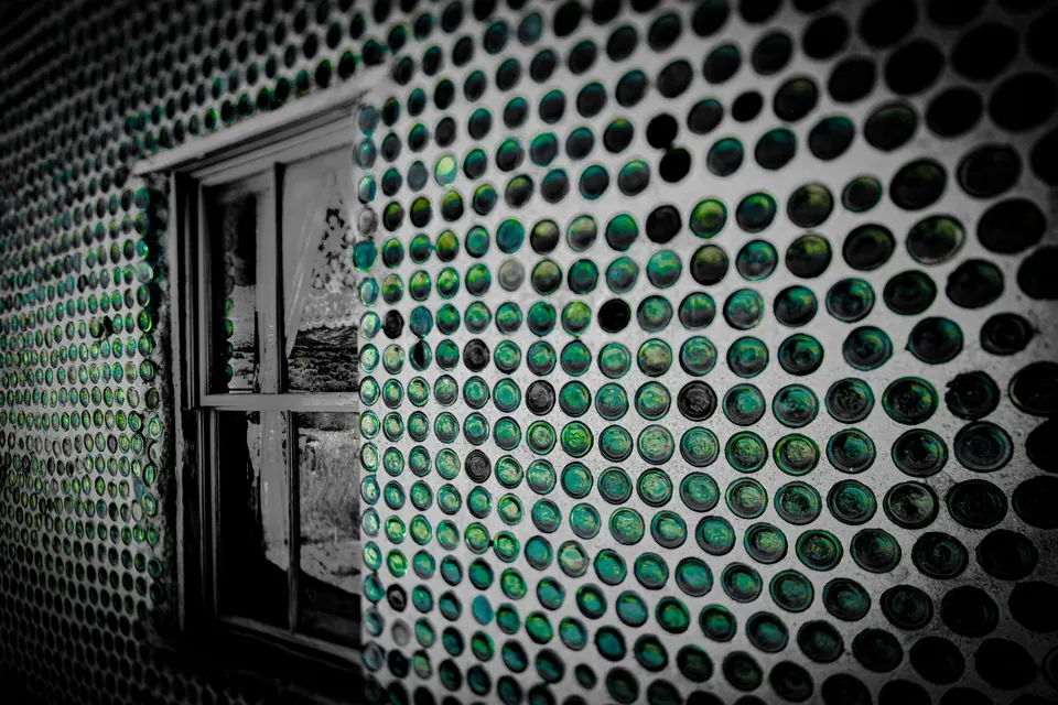 Rows of green glass bottles embedded in a wall surround a dark doorway.