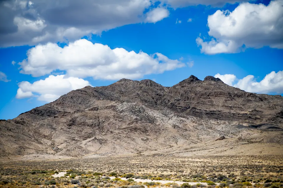 Bright clouds move over a rugged mountain range and a pale desert plain.