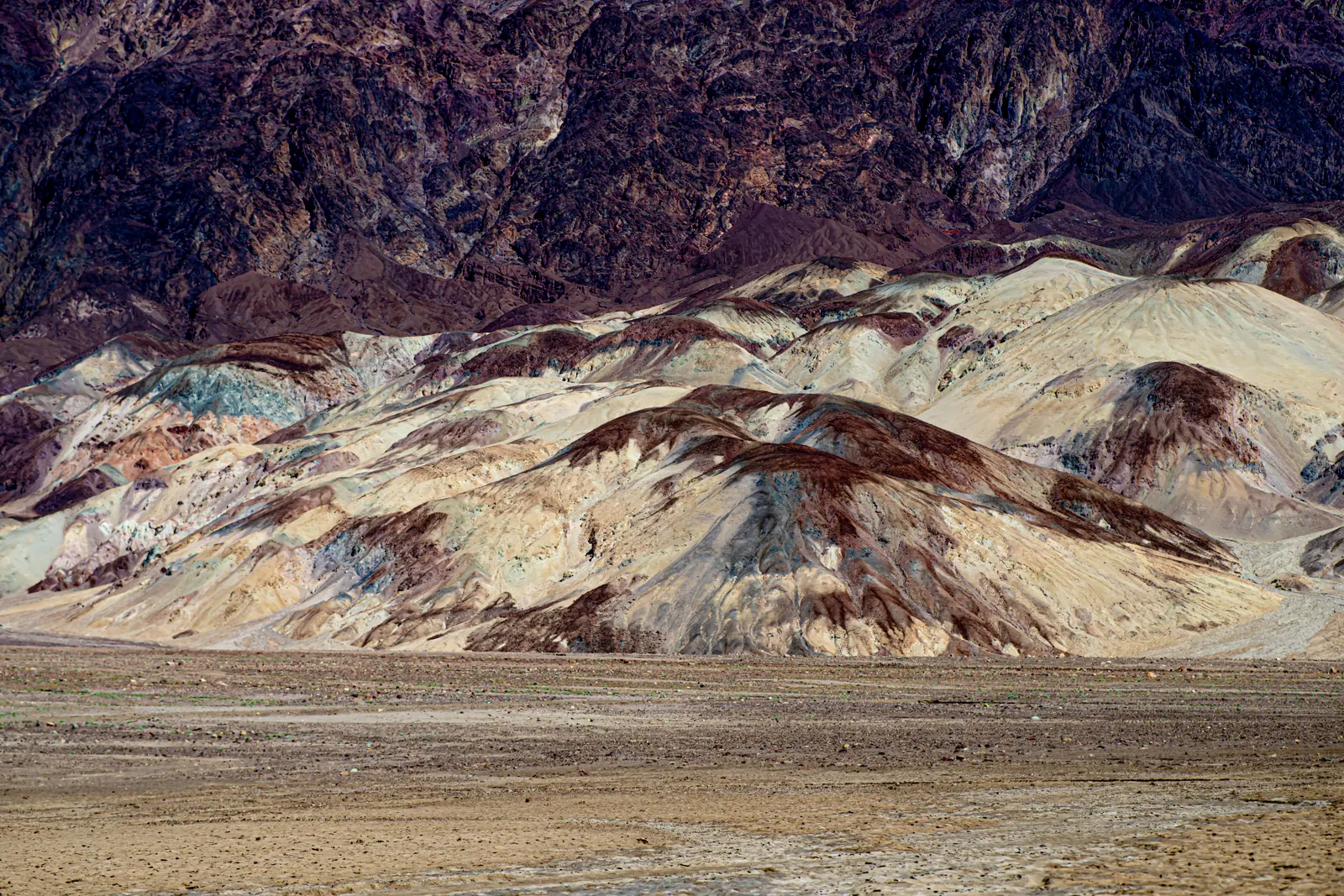 Pale yellow, pink and grey rock layers spread below a dark mountain wall.