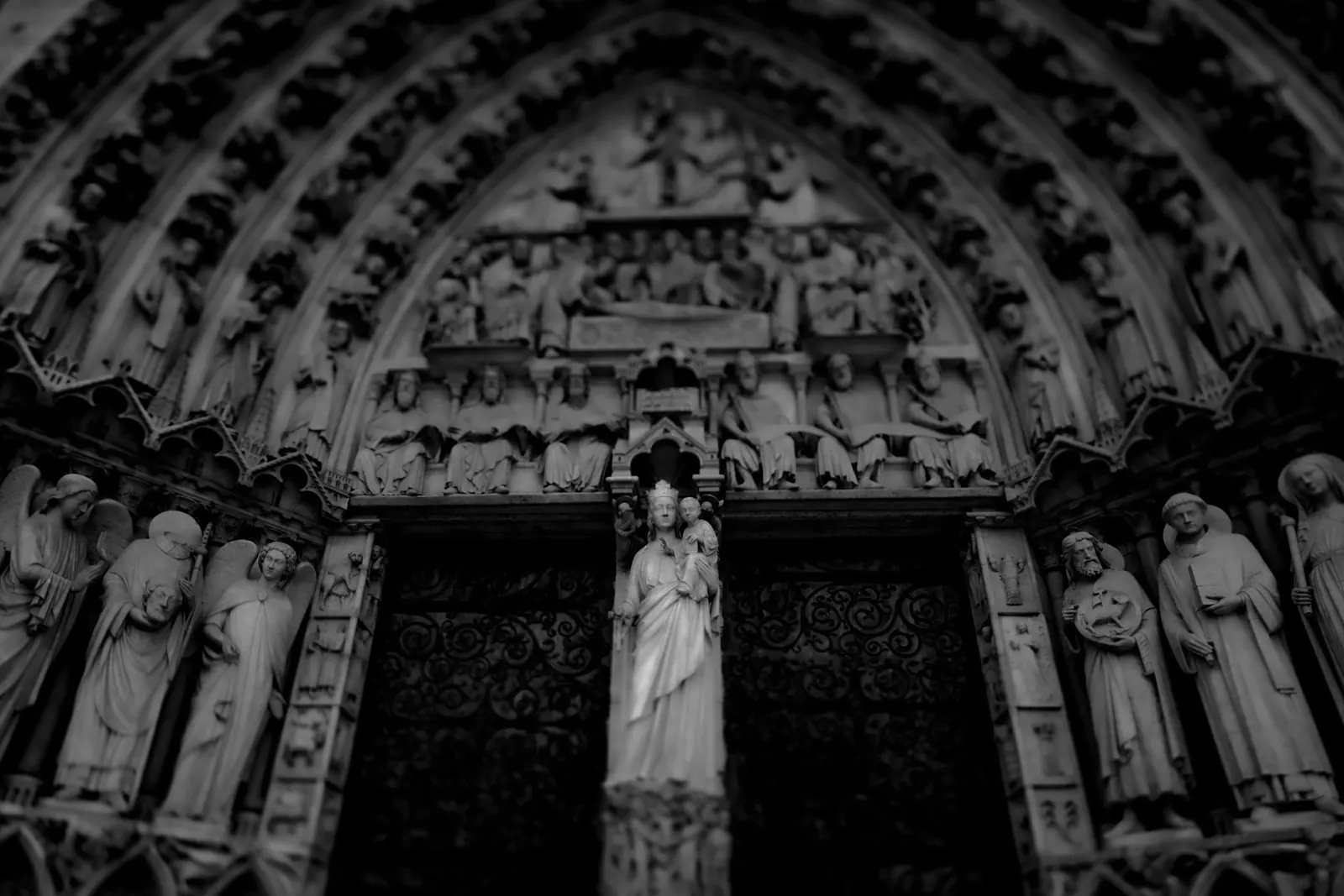 Carved figures surround the dark entrance of a cathedral in black and white.