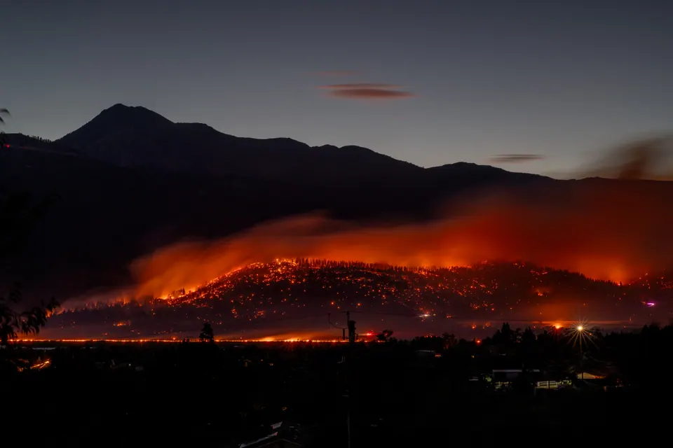 A long band of orange fire glows across a dark hillside at night.