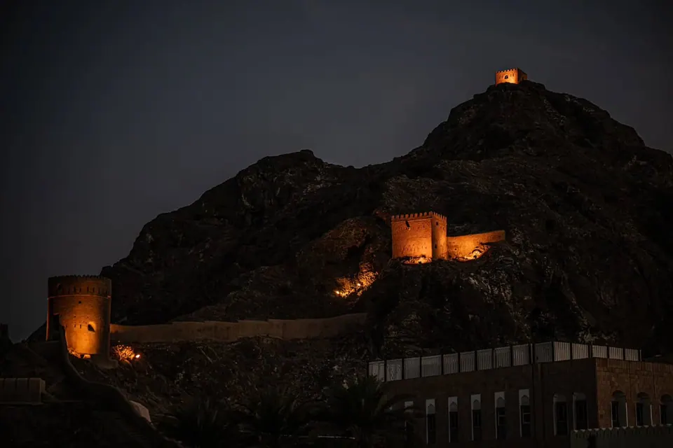 Warm lights trace a fort and its towers along a dark hillside.