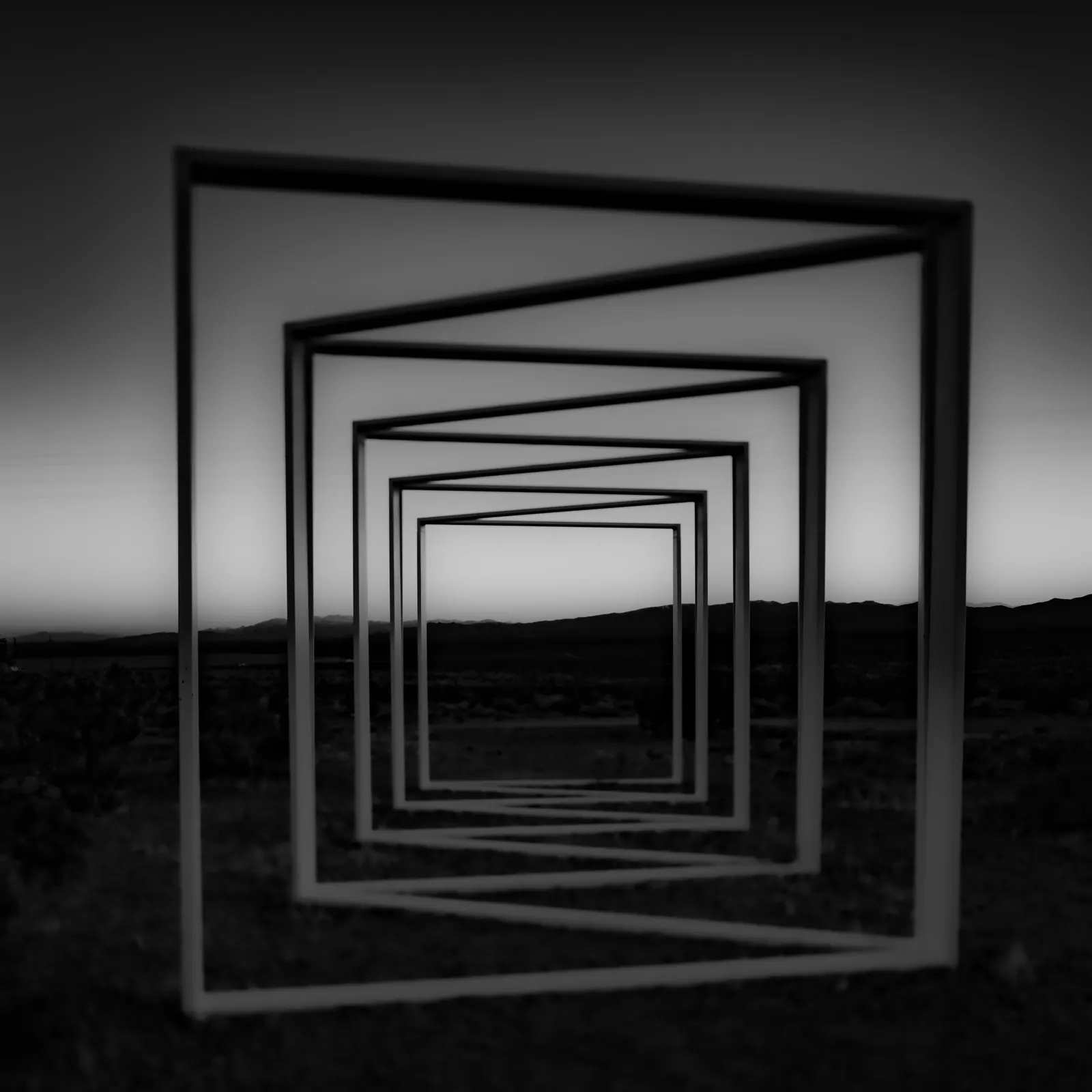 Repeating rectangular sculptures recede across a desert landscape in black and white.
