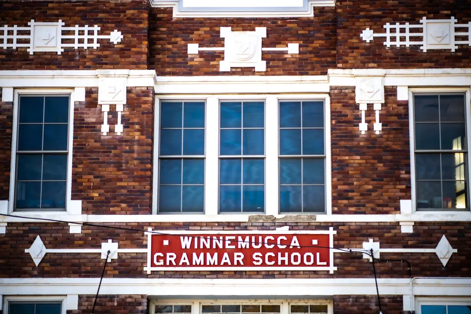 Blue windows and a school sign interrupt a patterned red and white brick facade.