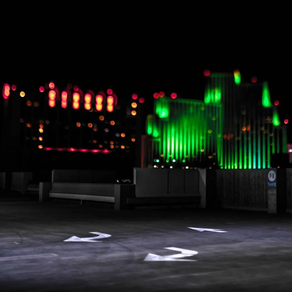 Green and red lights illuminate a building beyond an empty parking space.