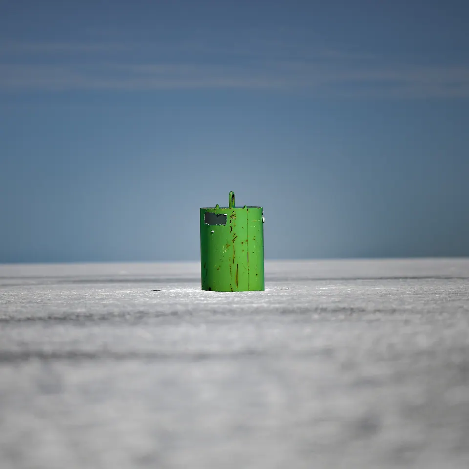 A small bright green structure stands alone on a vast pale frozen surface.