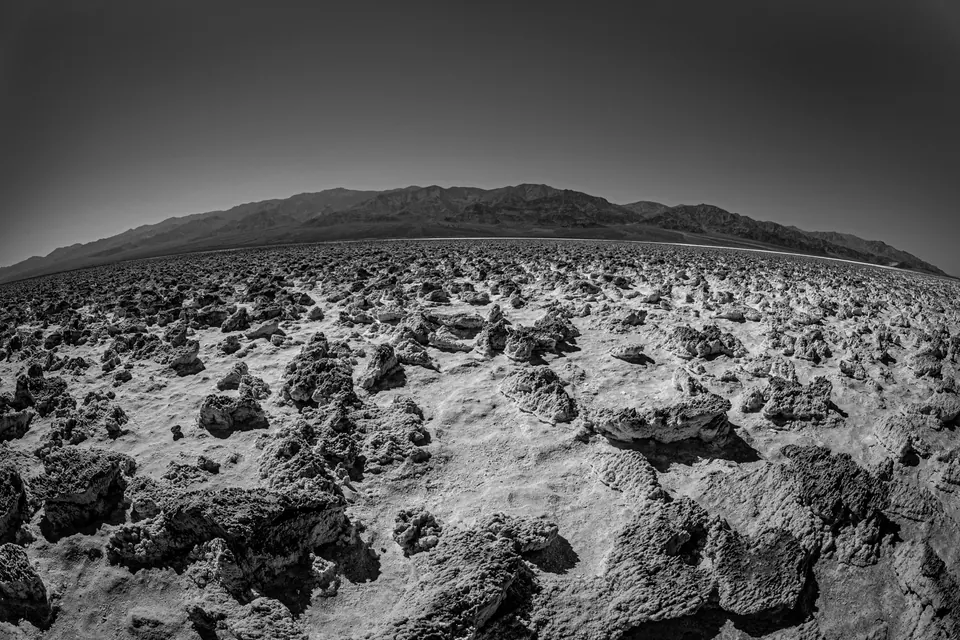 Rough, pale salt formations stretch toward a low ridge in black and white.