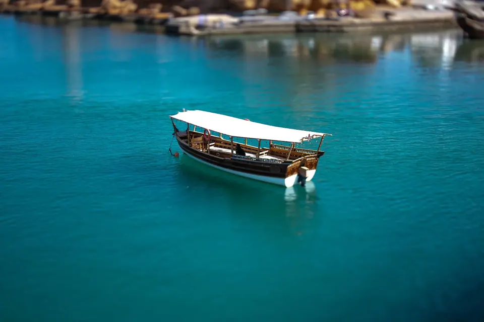 A small covered boat floats on clear turquoise water beside a rocky shore.