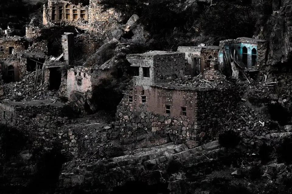 Abandoned stone houses and empty windows climb a steep rocky slope.