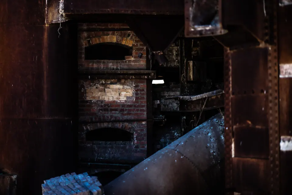 Rusted machinery and brickwork fill the dark interior of an abandoned industrial site.