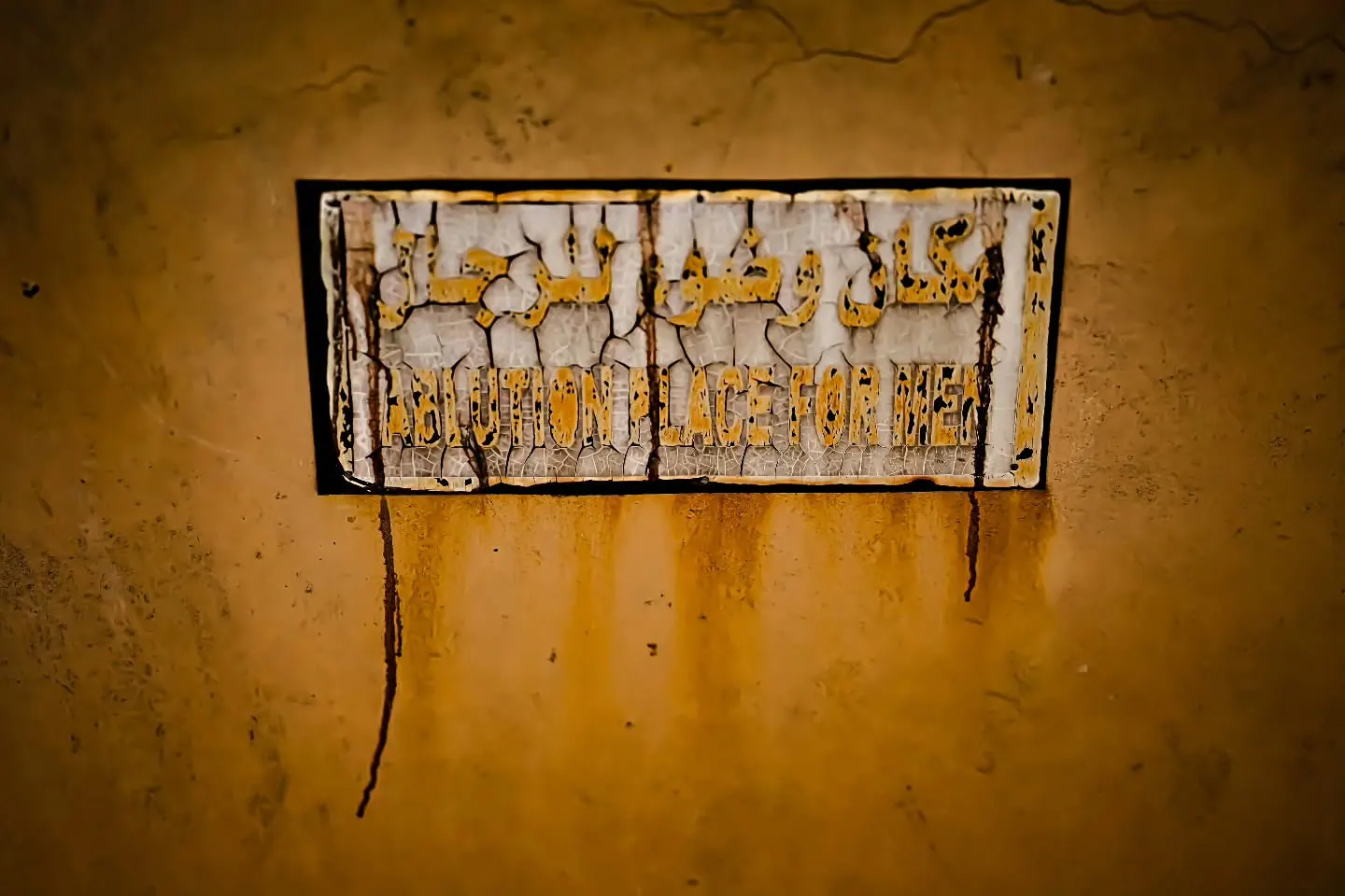 A weathered sign with painted lettering hangs on a rough ochre wall.
