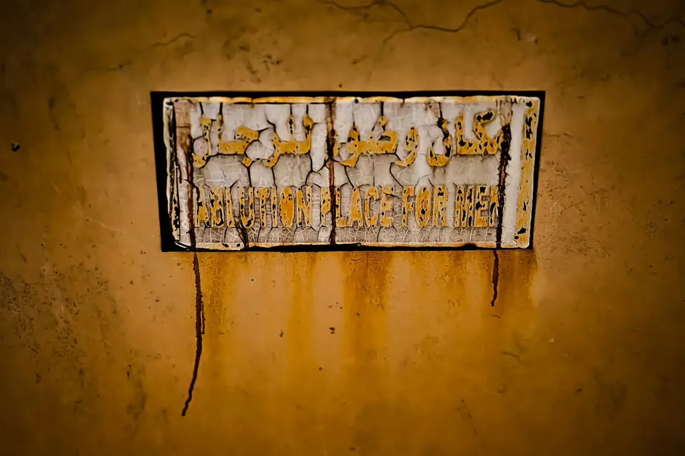 A weathered sign with painted lettering hangs on a rough ochre wall.