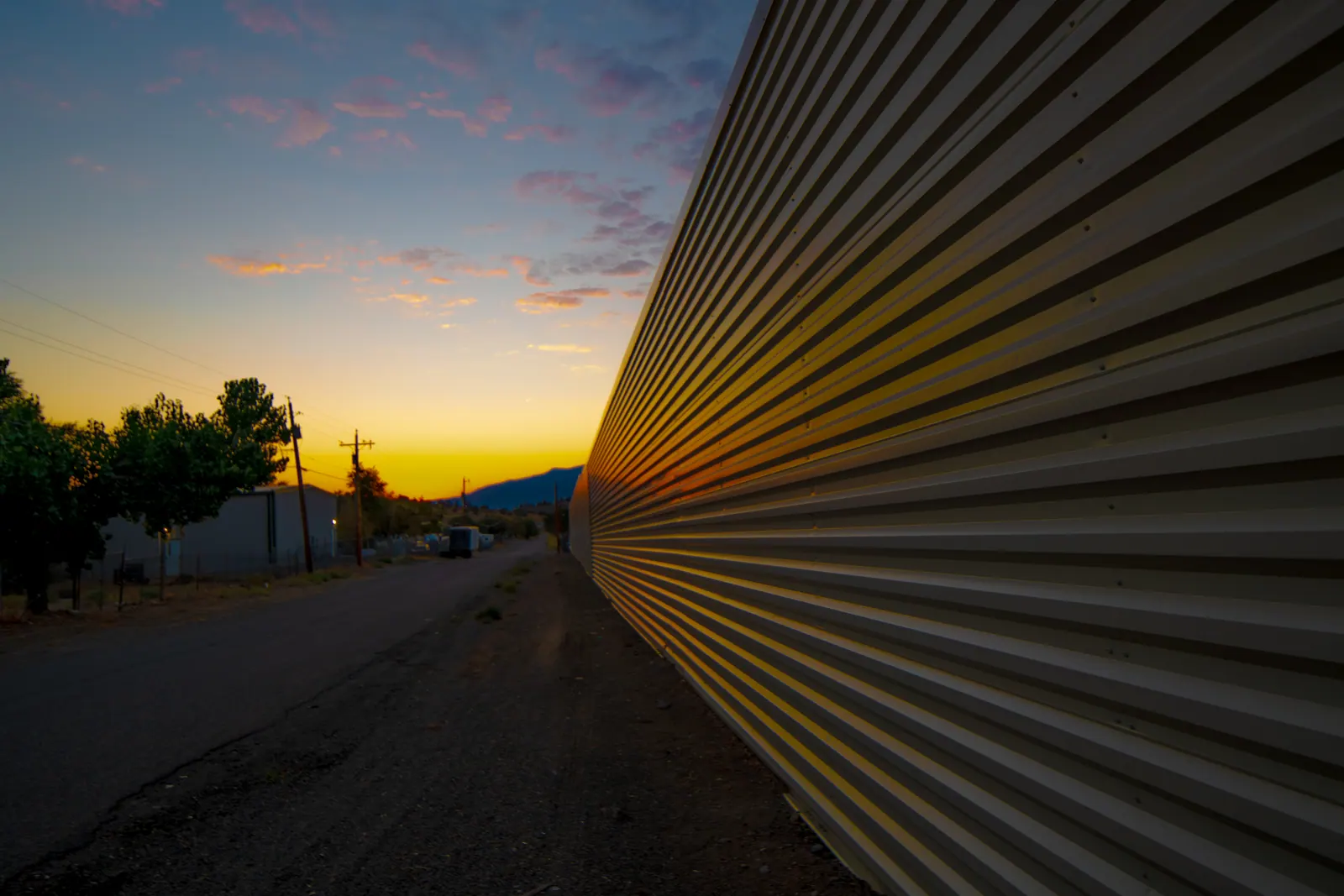 A sunset runs beside the long ribbed wall of an industrial building.