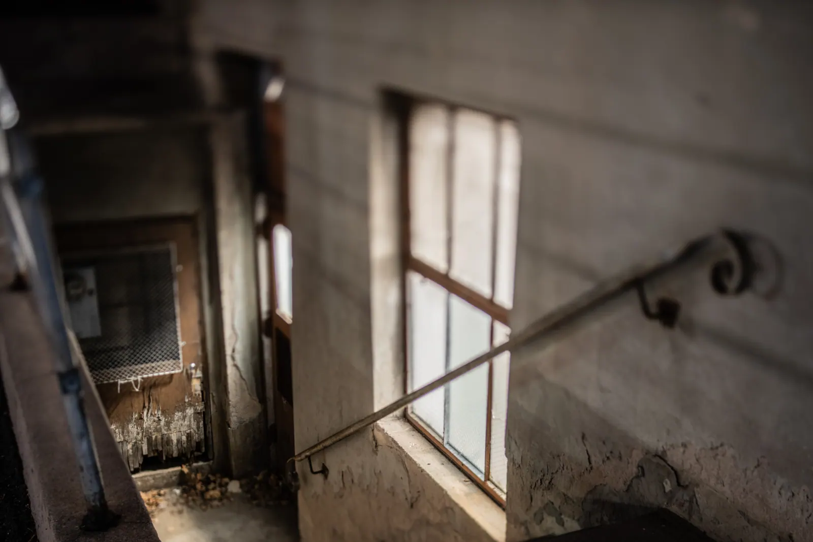A bright window throws light into a worn stairwell with peeling walls and a simple handrail.