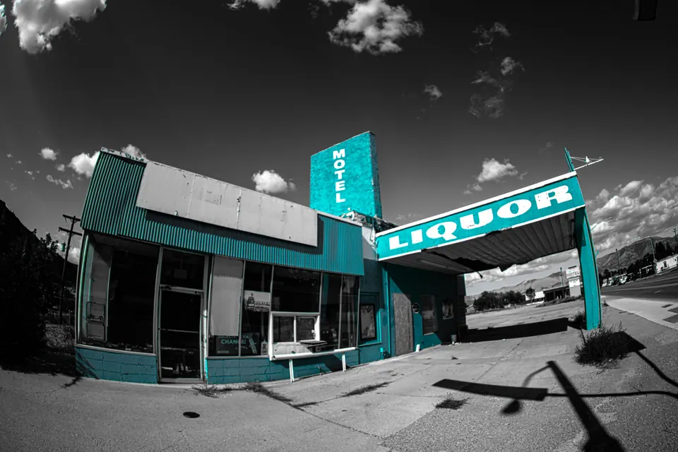 Turquoise motel and liquor signs stand above an empty street under bright clouds.