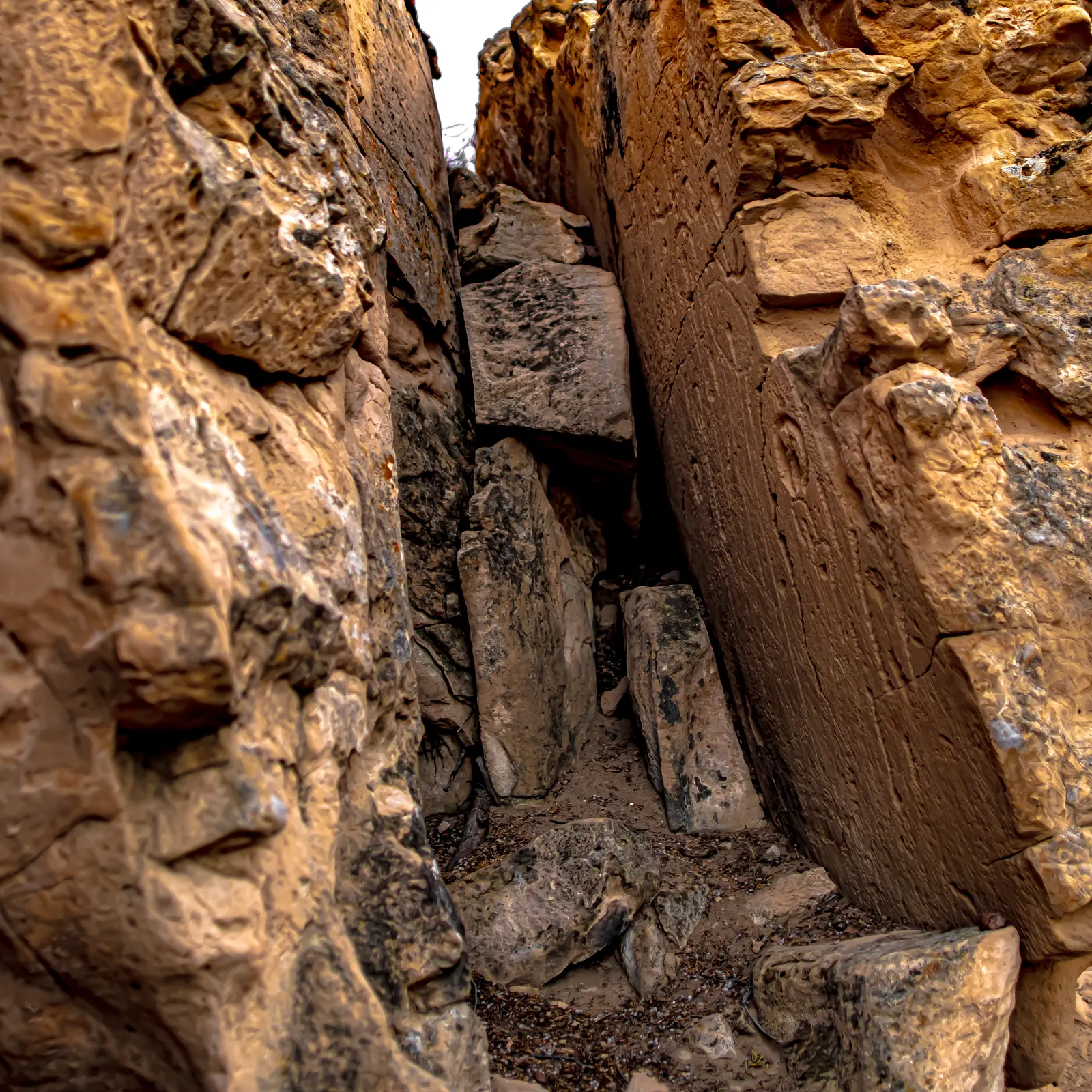 A narrow upright slab with carved markings stands between warm, rough rock walls.