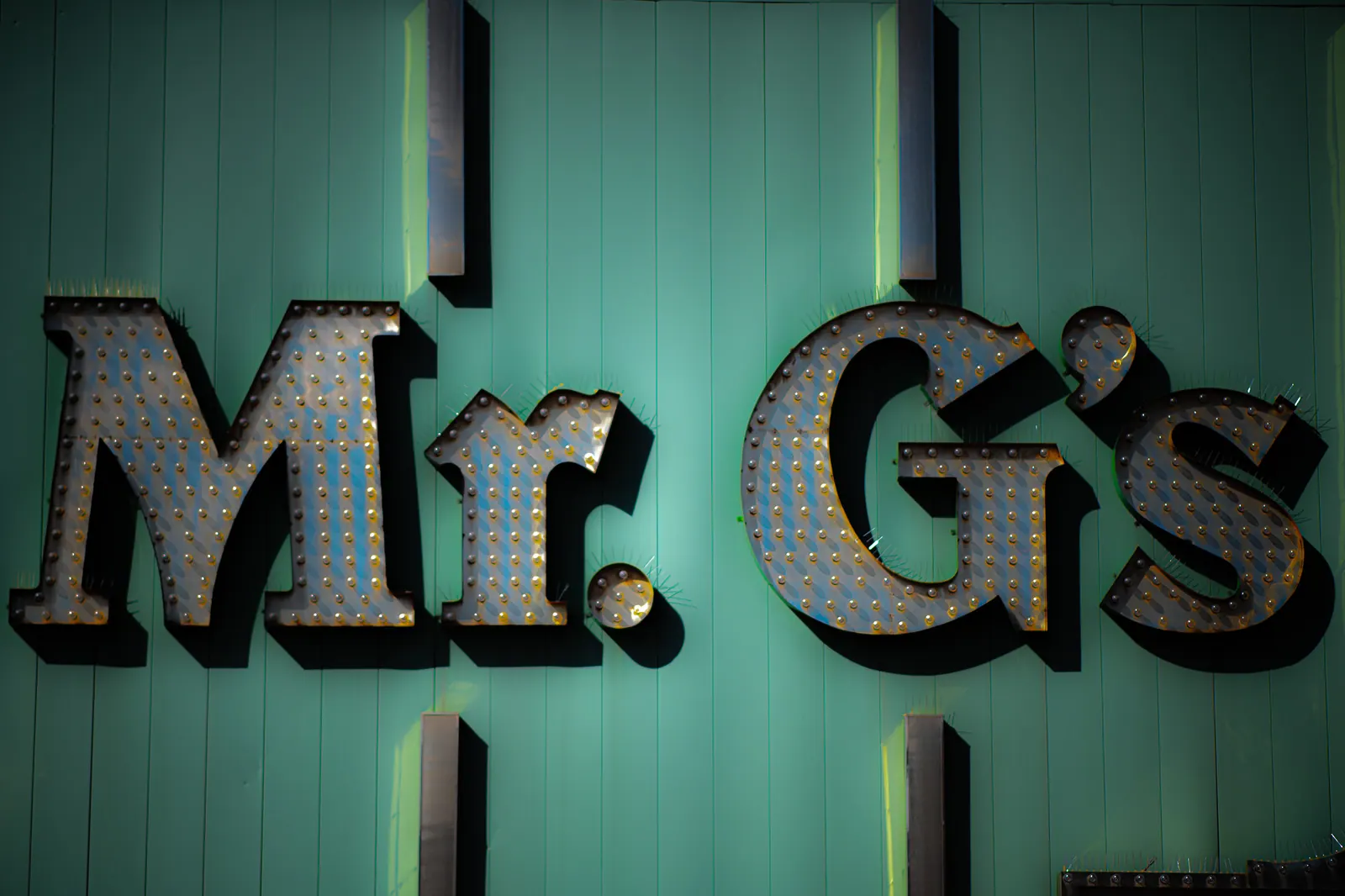 Large weathered letters hang against a turquoise wall in angled light.