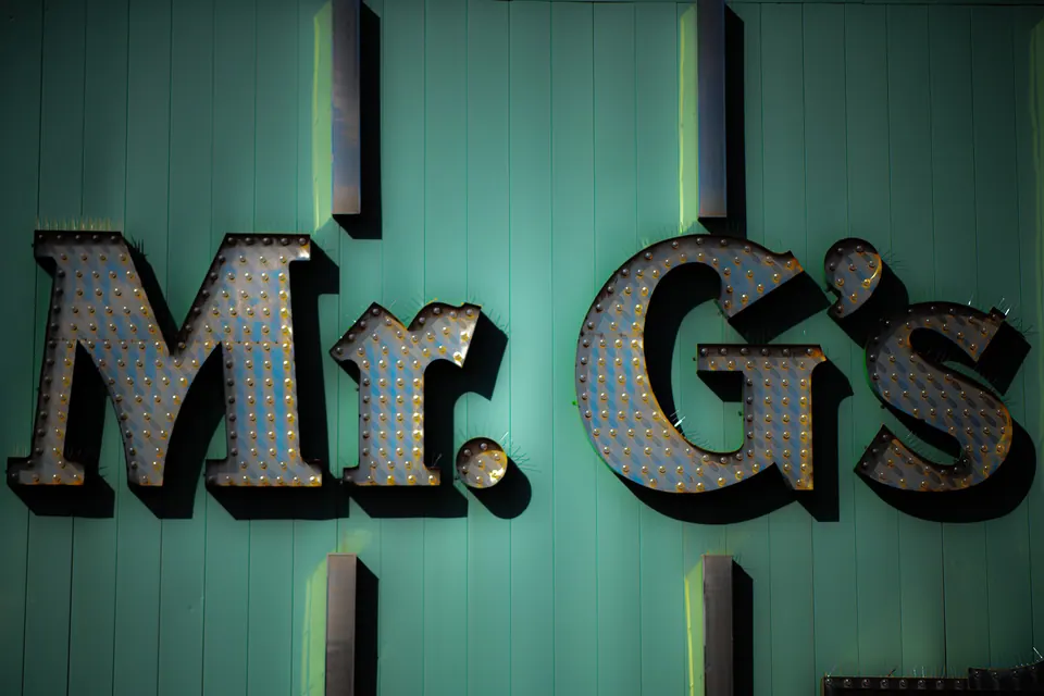 Large weathered letters hang against a turquoise wall in angled light.