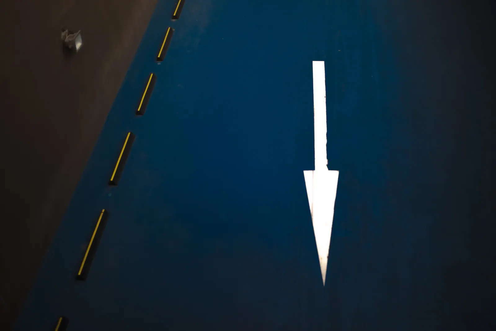 A white arrow points along a blue lane crossed by yellow road markings.