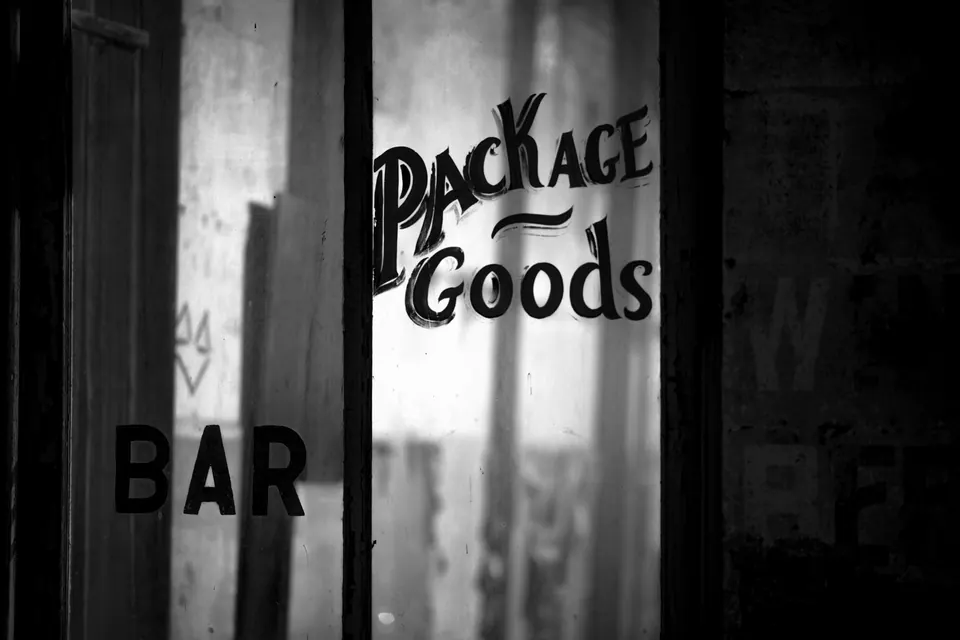 Faded bar lettering on glass is framed by dark wood and reflected light.