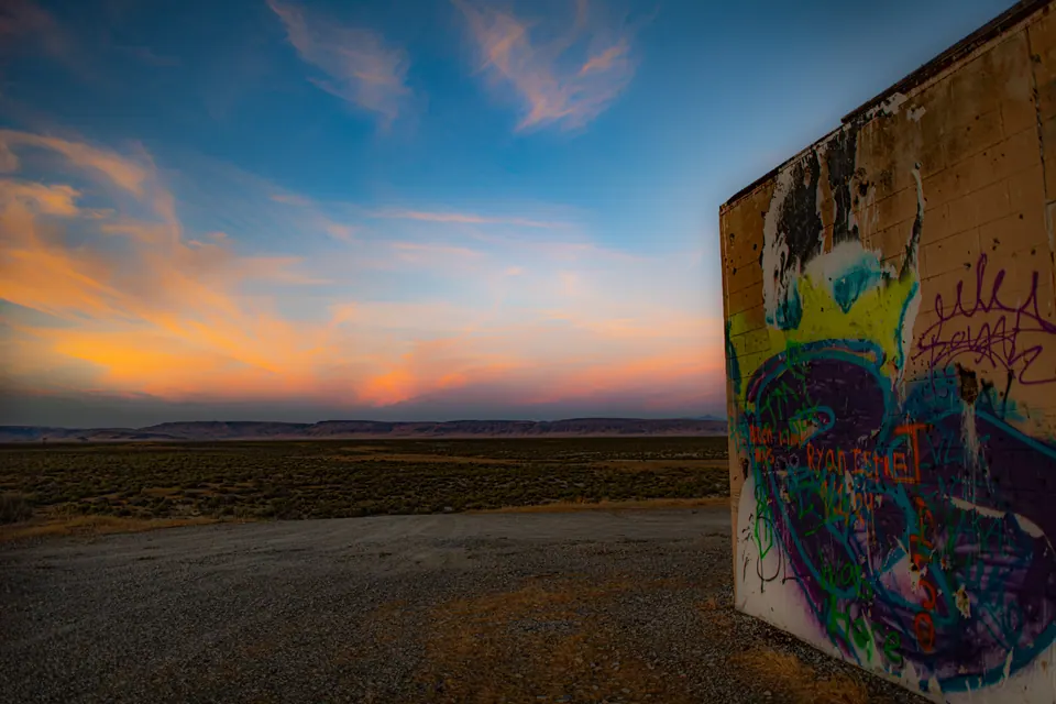 A painted concrete wall stands beside open land under a colourful evening sky.