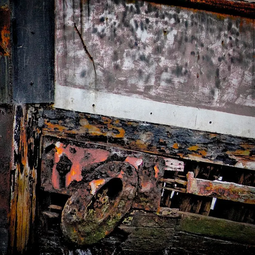 Layers of pink, yellow and grey paint peel from an old metal surface.
