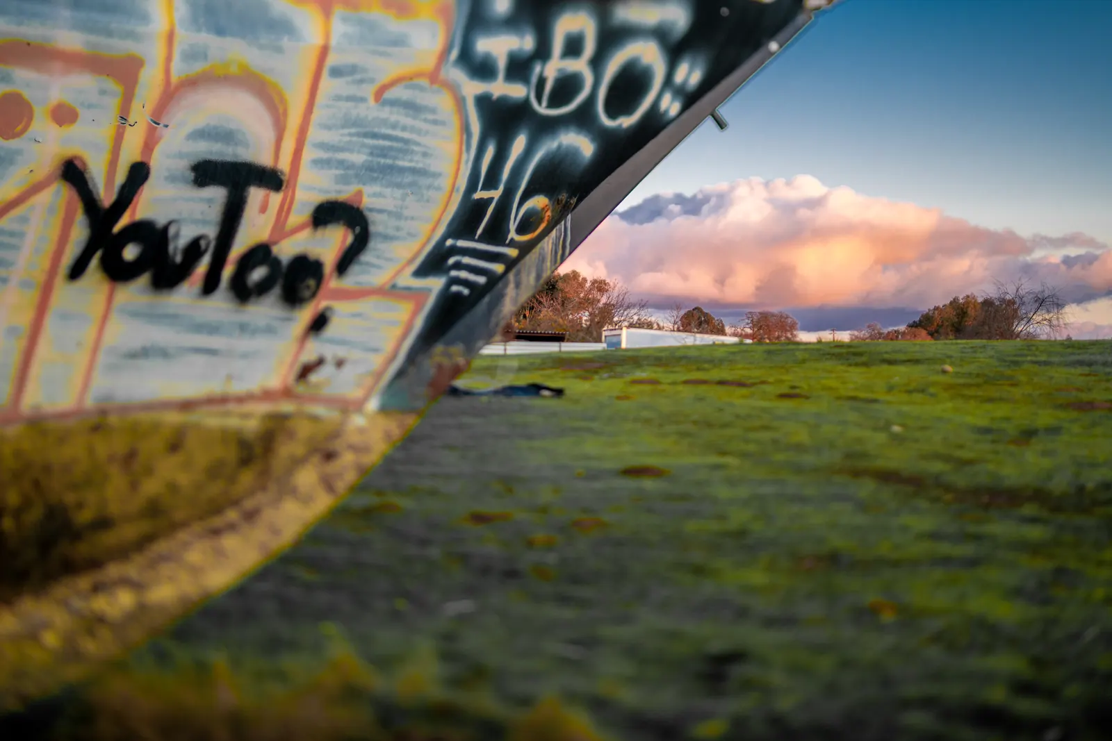 A graffiti-covered concrete structure stands beside green grass under a bright sky.