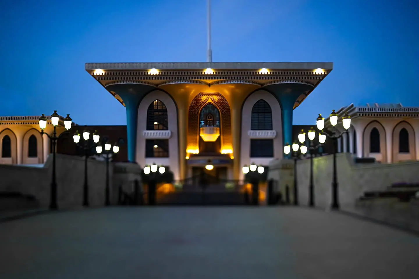 A brightly lit palace entrance stands beneath a deep blue evening sky.