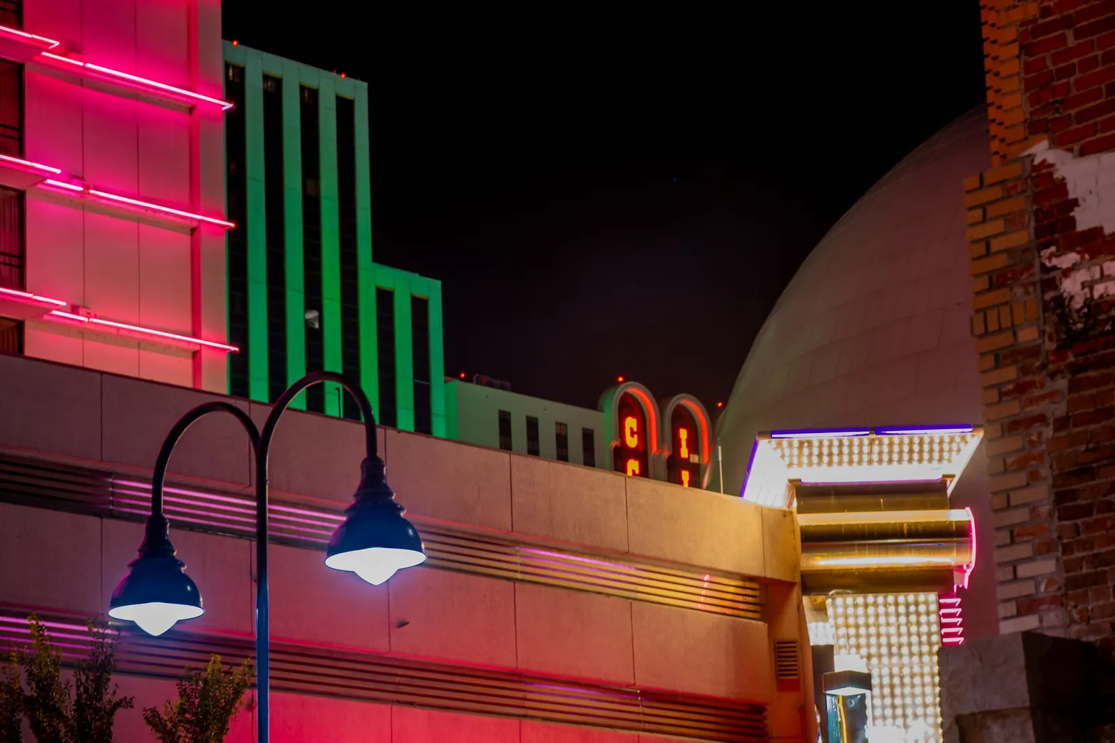Bright pink and green architectural details illuminate a city facade after dark.