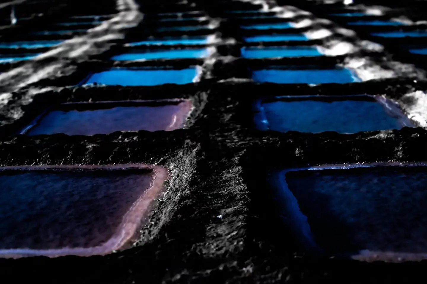 Small rectangular pools reflect blue and violet light among dark stone edges.