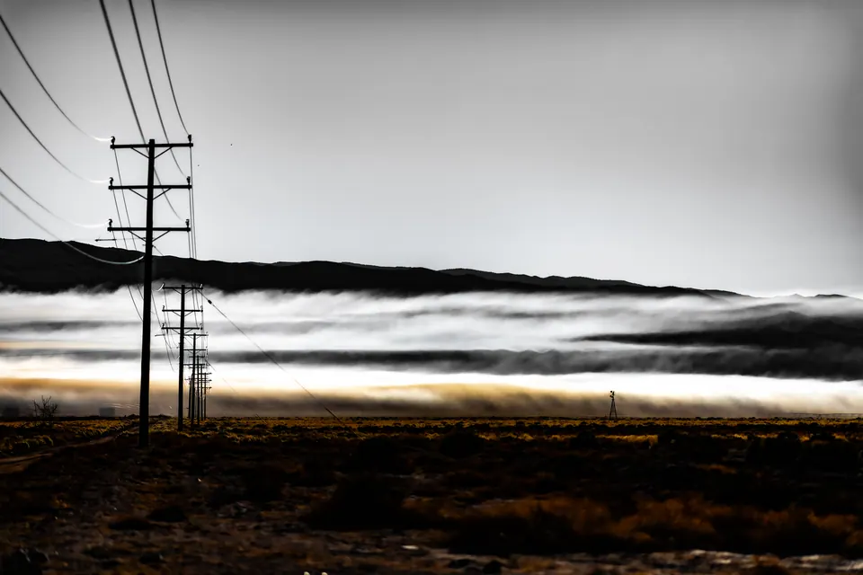 Utility poles cross a dark valley filled with a low band of white mist.