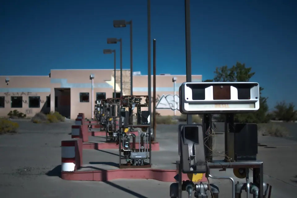 Old fuel pumps stand in an empty forecourt beneath a blue sky.