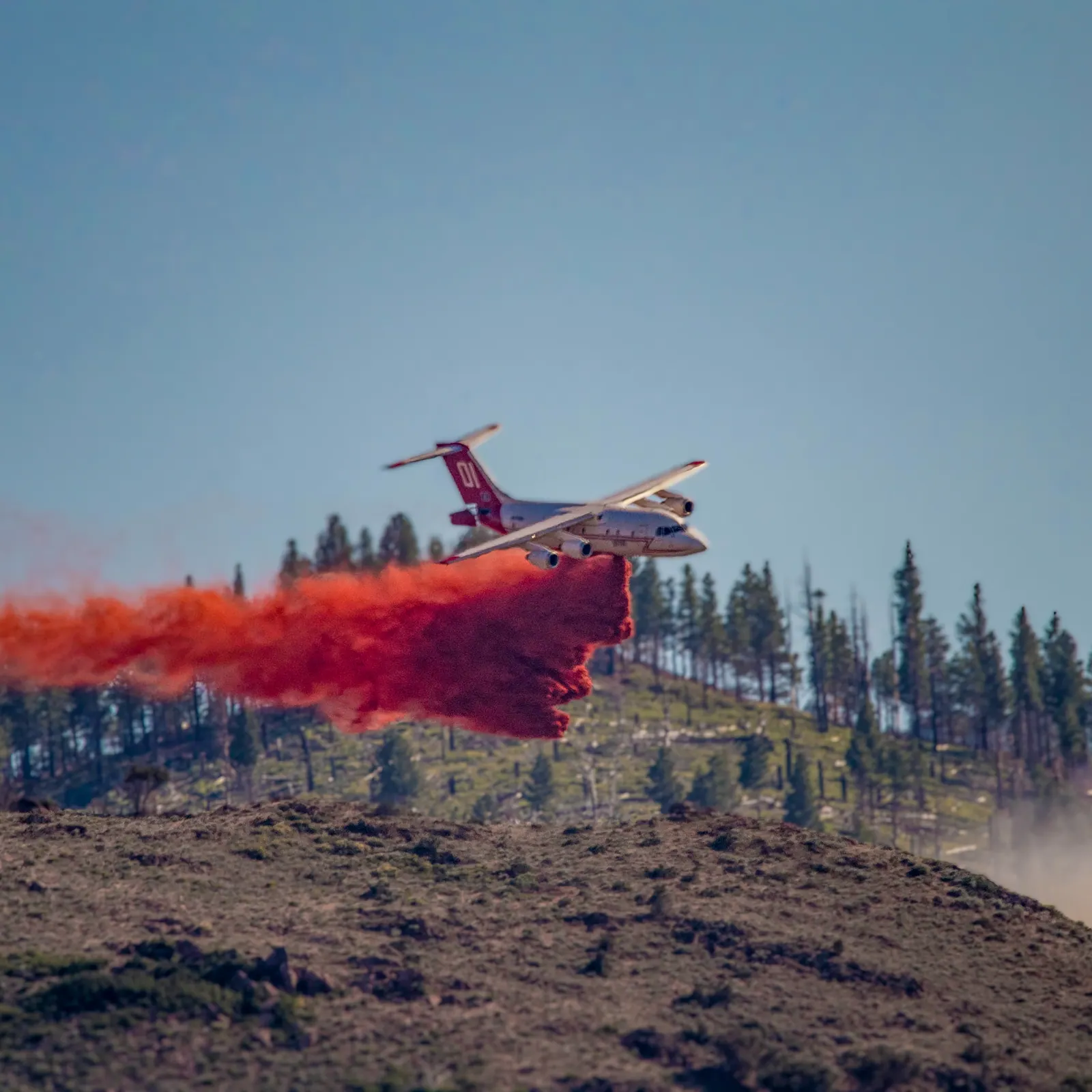 An aircraft drops a bright red plume above a wooded hillside.