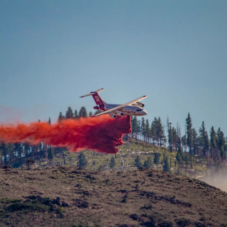 An aircraft drops a bright red plume above a wooded hillside.